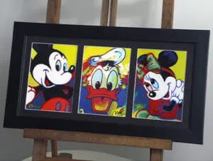 A triptych sitting on an easel of Donald Duck with Mickey and Minnie Mouse painted in pop art cartoon style.